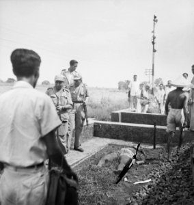 Een lijk ligt op de grond bij een betonnen bak (tunnel, schuilkelder Om hem , Bestanddeelnr 15557