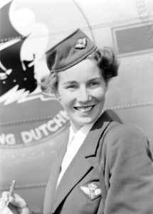 Een KLM stewardess poseert voor een vliegtuig met het Flying Dutchman embleem, Bestanddeelnr 255-8955