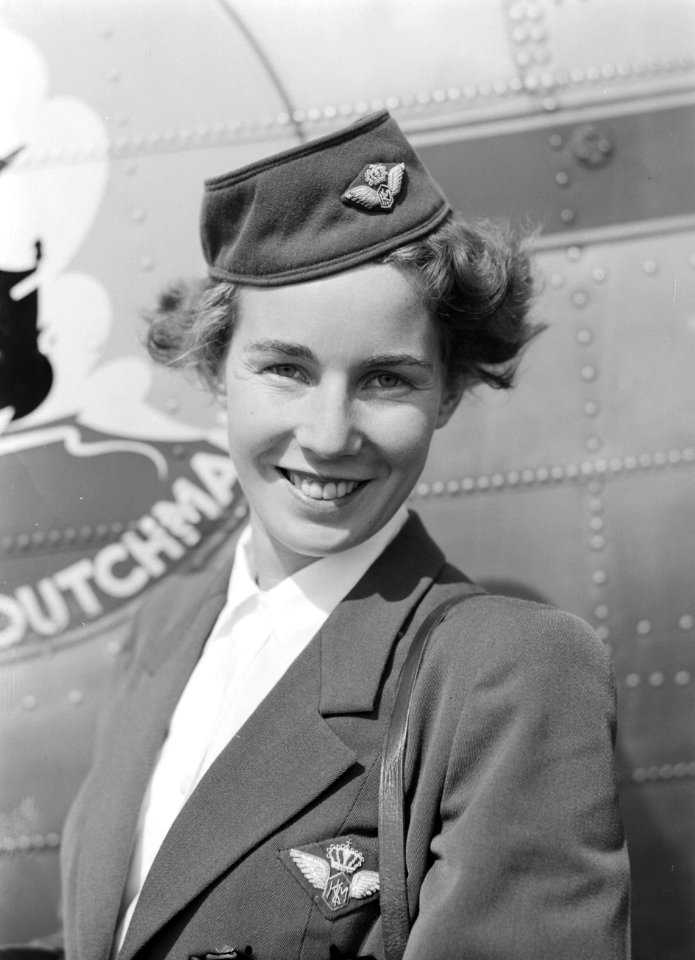 Een KLM stewardess poseert voor een vliegtuig met het Flying Dutchman embleem, Bestanddeelnr 255-8956