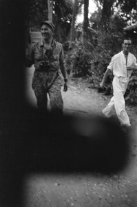 Een lachende militair in camouflagepak en een man in witte kleding, Bestanddeelnr 324-6-6