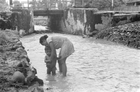 Een kind wordt gewassen in een beek Daarachter is een sluisbrug te zien, Bestanddeelnr 456-6-5