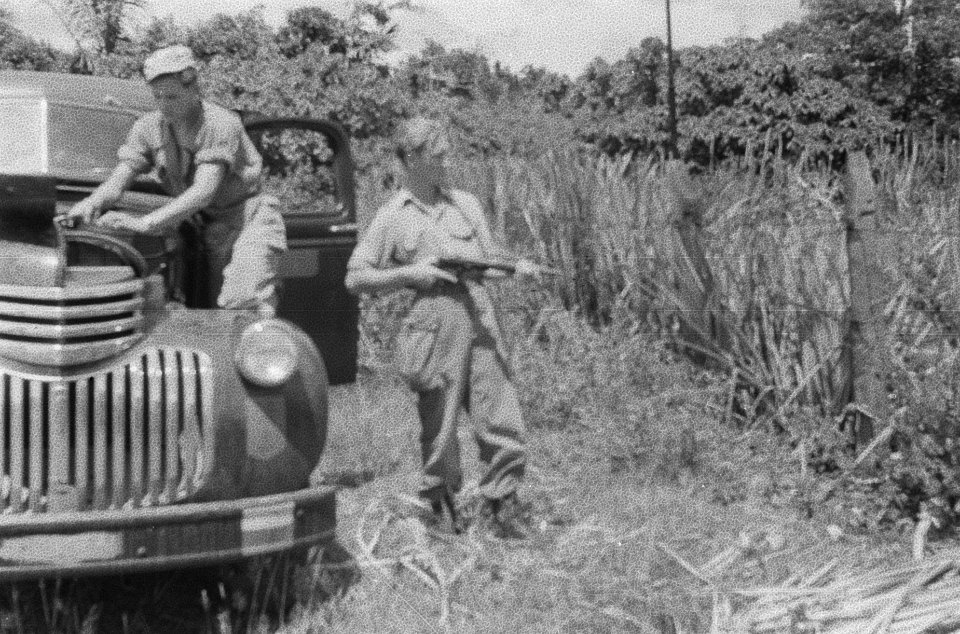 Een militair is bezig met de motor van een auto, terwijl een tweede met stengun , Bestanddeelnr 382-6-1