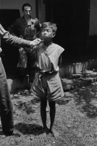 Een militair houdt een vinger onder de kin van een jonge Indonesische jongen, di, Bestanddeelnr 349-3-1