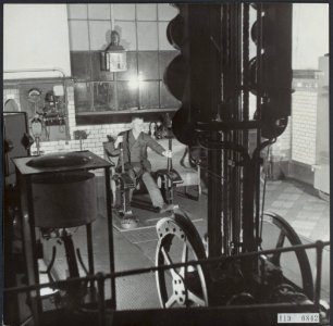 Een machinist bedient het mechanisme voor liften. Voor hem staat een groep verke, Bestanddeelnr 119-0842