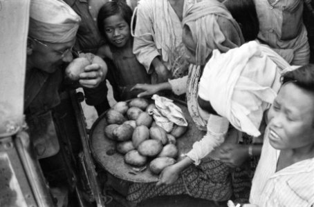 Een militair in de laadbak van een voertuig ruikt aan een mango Voor hem een ma, Bestanddeelnr 482-1-3