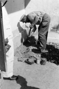 Een man in uniform met pet graaft objecten op. Rechts staan er enkele (mijnen, b, Bestanddeelnr 285-4-6