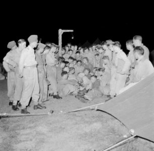 Een militair leest 's avonds een spannend verhaal voor in het Morib Beach-kamp o, Bestanddeelnr 255-8269