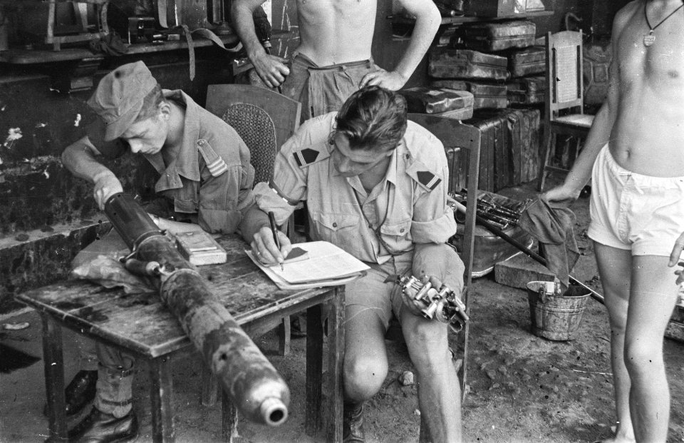 Een militair ( schouderepauletten onbekend) noteert iets in een schrift terwijl, Bestanddeelnr 458-2-3