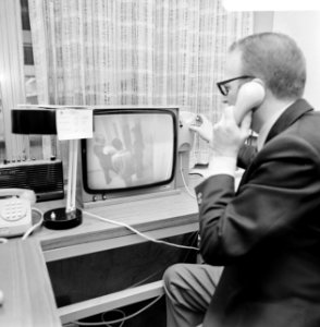 Een medewerker aan de telefoon achter het beeldscherm, Bestanddeelnr 926-9151