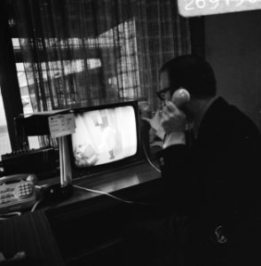 Een medewerker aan de telefoon achter het beeldscherm, Bestanddeelnr 926-9150
