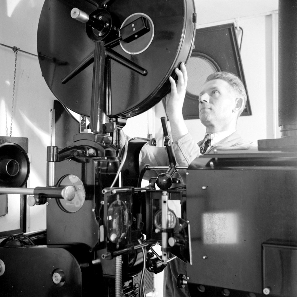 Een personeelslid plaats een film in de projector, Bestanddeelnr 255-7792