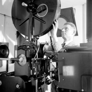 Een personeelslid plaats een film in de projector, Bestanddeelnr 255-7792