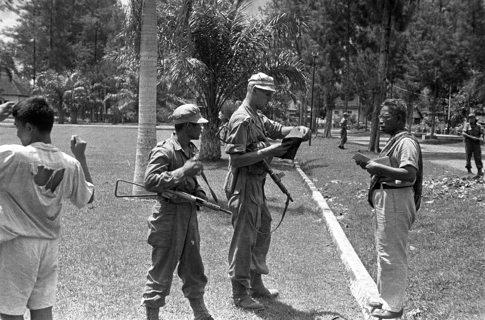 Een Nederlandse militair met een stengun controleert papieren die hem worden aan, Bestanddeelnr 5727