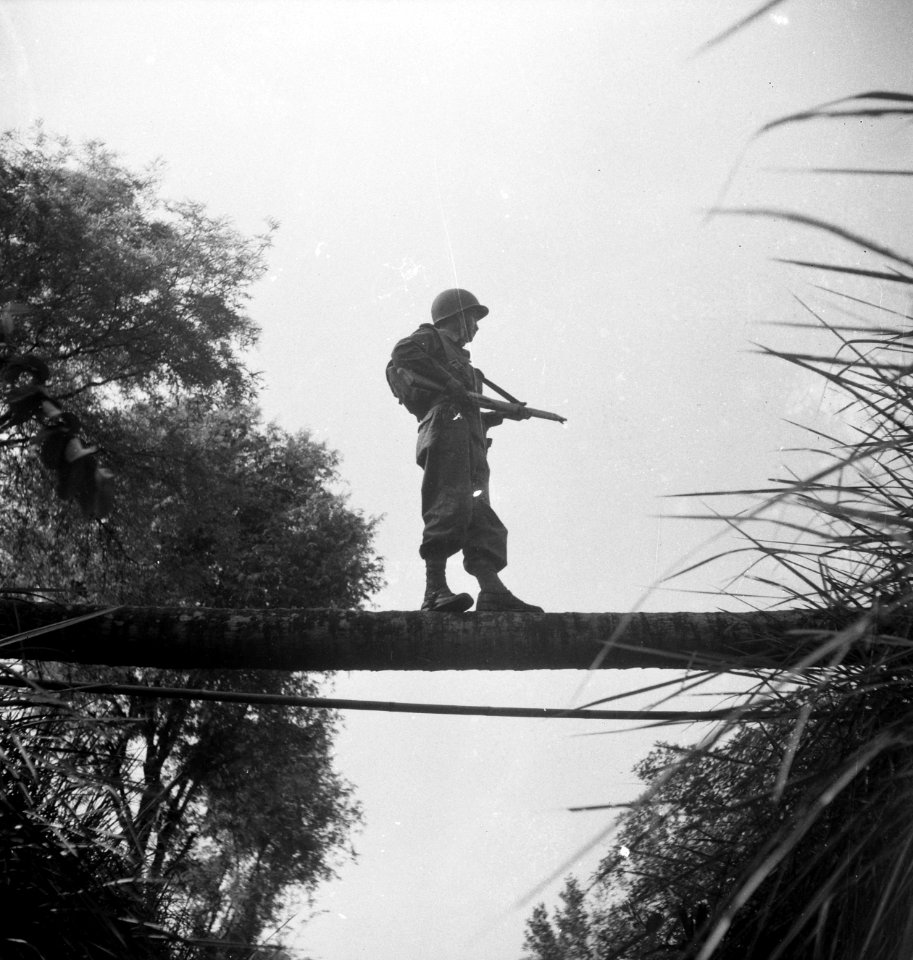 Een militari taat op een boomstam over een beek of sloot, met zijn wapen gerich…, Bestanddeelnr 15813