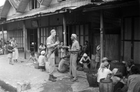 Een Nederlandse militair spreekt met een Indonesische man. Om hen heen zitten m, Bestanddeelnr 3087