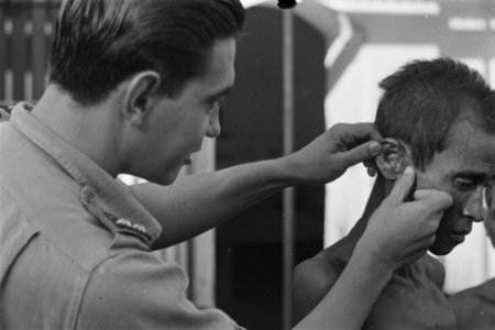 Een Nederlandse militaire arts controleert de oren van een Indonesische man, Bestanddeelnr 125A-4-6