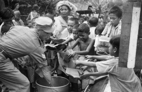Een Nederlandse militair deelt eten uit. Kinderen en een vrouw reiken bananenbla, Bestanddeelnr 470-5-4