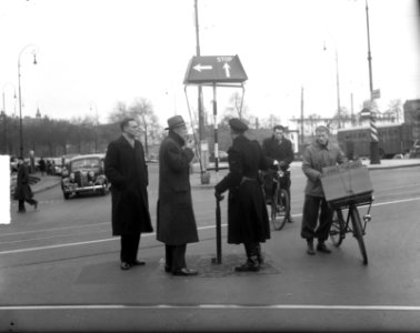 Een politieagent met een verkeersaanwijzer in gesprek met twee mannen, Bestanddeelnr 934-7074