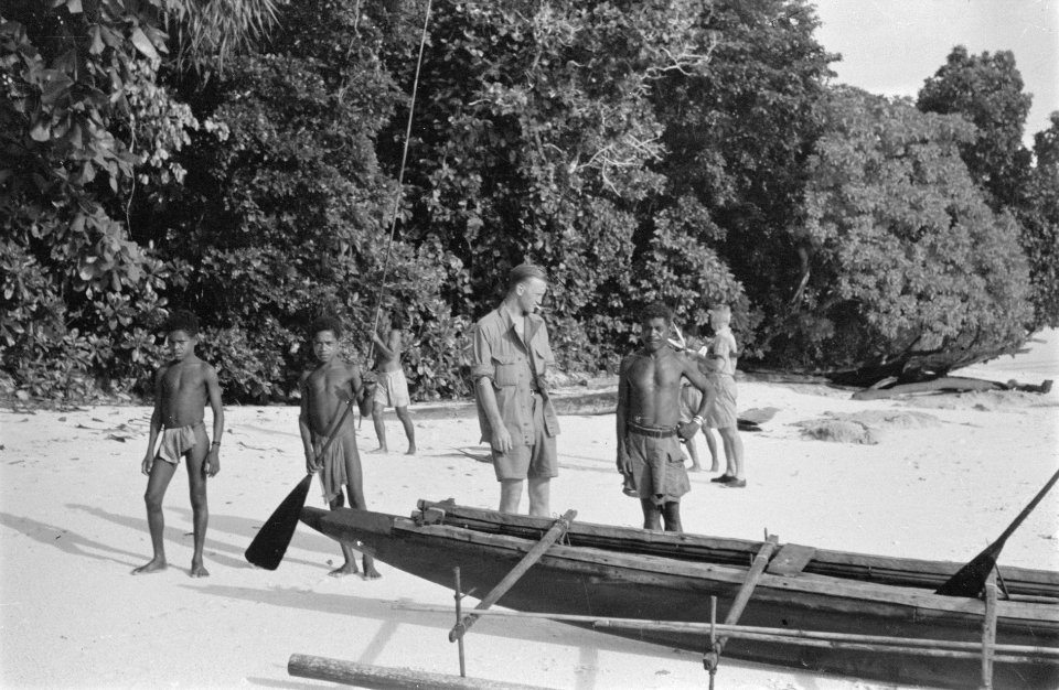 Een Nederlandse man op een strand. Bij hem staan drie lokale inwoners, een man e, Bestanddeelnr 438-6-3