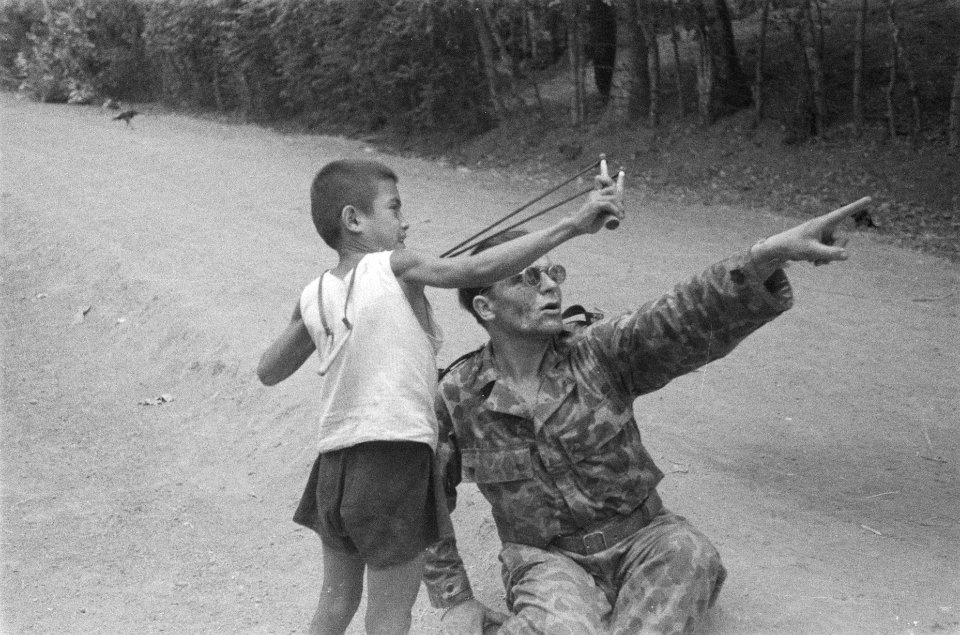 Een Public Relation man leert een Indonesische jongen om te gaan met een katapul, Bestanddeelnr 75-5-3