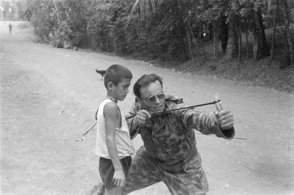 Een Public Relation man leert een Indonesische jongen om te gaan met een katapul, Bestanddeelnr 75-5-6