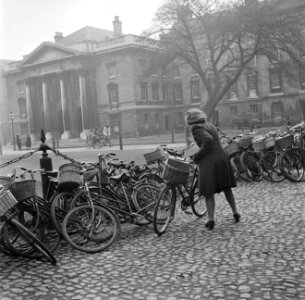 Een studente moet andere fietsen opzij zetten, op de binnenplaats van het Trinit, Bestanddeelnr 191-0860