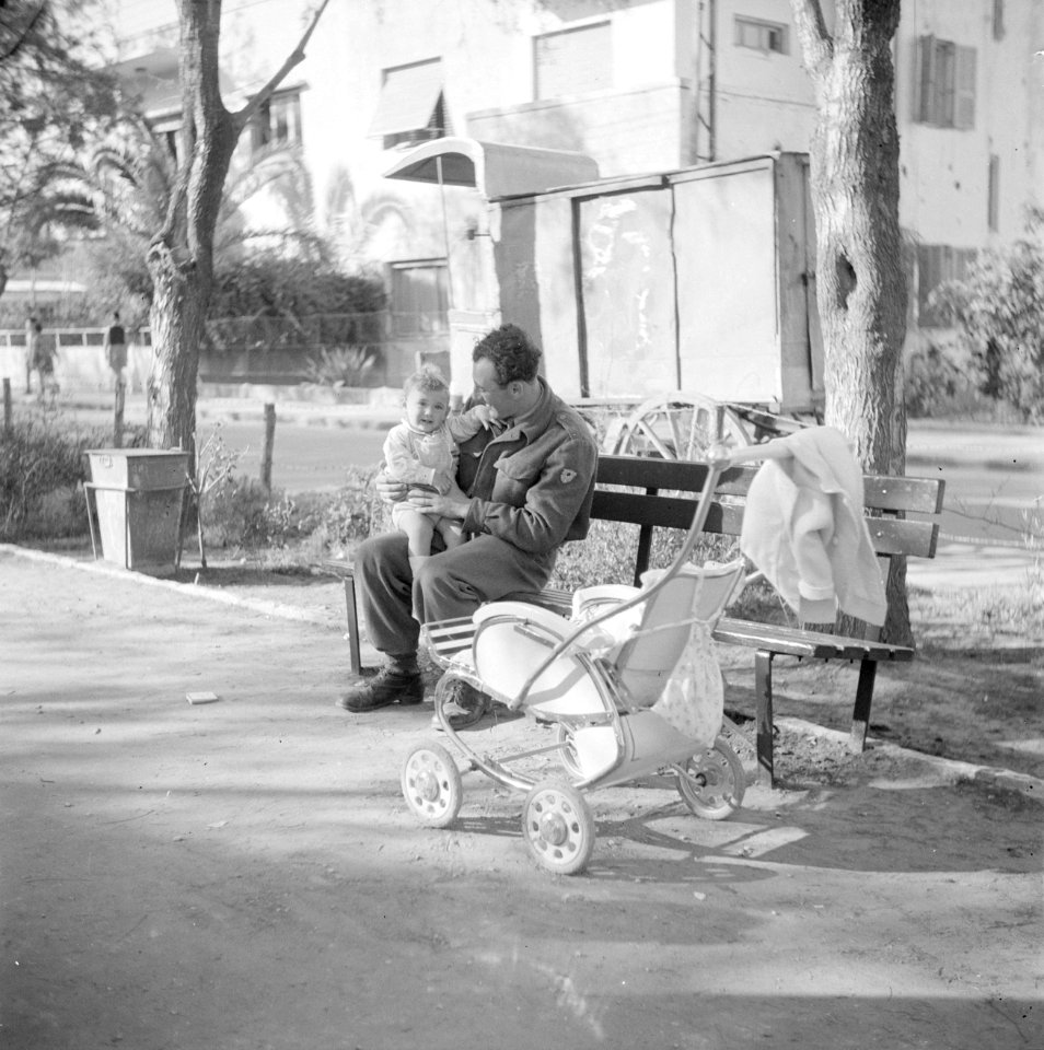 Een soldaat met verlof op een bank in een park in Tel Aviv met zijn kind op sch…, Bestanddeelnr 255-1290