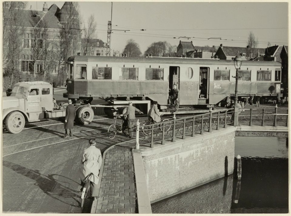 Een tram zonder wielen passeert tijdens het vervoer daarvan de Emmabrug, op weg naar de NZH remise aan de Leidsevaart. NL-HlmNHA 54004235