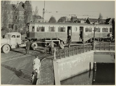 Een tram zonder wielen passeert tijdens het vervoer daarvan de Emmabrug, op weg naar de NZH remise aan de Leidsevaart. NL-HlmNHA 54004235