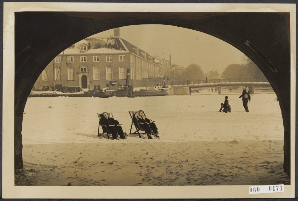Een tweetal dames nemen een zonnebad in het midden van de bevroren Amstel, Bestanddeelnr 060-0171