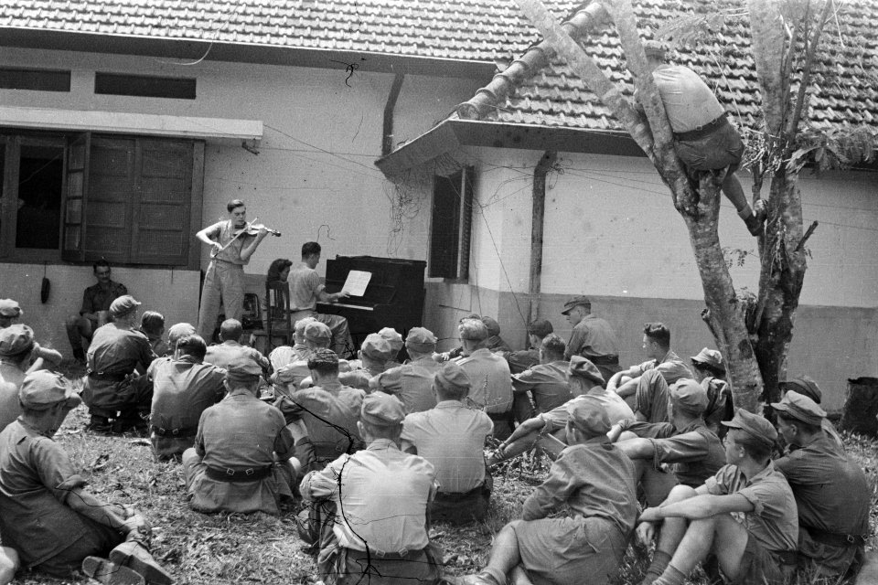 Een violist speelt, begeleidt door een pianist. Soldaten luisteren zittend, Bestanddeelnr 269-4-2