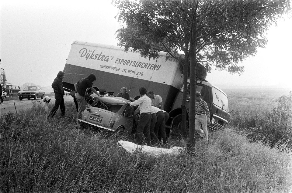 Een vernielde personenauto wordt door hulpverleners geholpen, met op de achtergr, Bestanddeelnr 928-0982