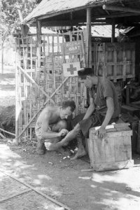 Een verpleegkundige van een Rode Kruispost behandelt het been van een man Op he, Bestanddeelnr 53-4-3