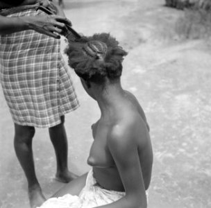 Een vrouw bezig met het maken van een kapsel in Langetabbetje in Suriname, Bestanddeelnr 252-6769
