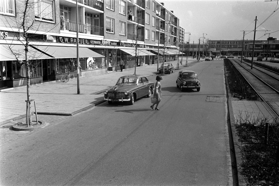 Een vrouw in laklederen regenjas met boodschappentas steekt over terwijl voor …, Bestanddeelnr 923-4338