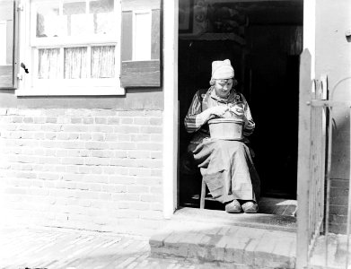 Een Marker meisje in klederdracht schilt aardappels in de deuropening, Bestanddeelnr 252-0686