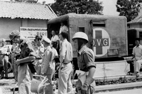 Een ambulance met rood kruis en opschrif O.V.G. staat bij een steen- & Dakpan…, Bestanddeelnr 2254