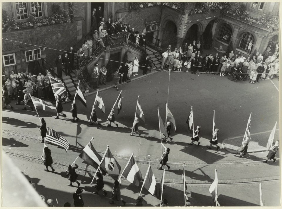 Een allegorische optocht op de Grote Markt tijdens de Kroningsweek passeert het Stadhuis. NL-HlmNHA 54004436