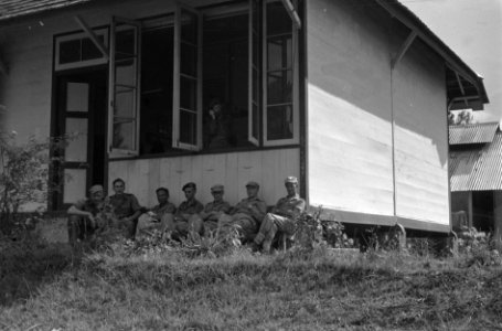 Een groep officieren rust uit en en zit in de schaduw van een houten huis of bar, Bestanddeelnr 5282