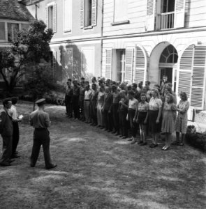 Een groep mannen, en enkele vrouwen, staan aangetreden voor een huis, Bestanddeelnr 900-5907