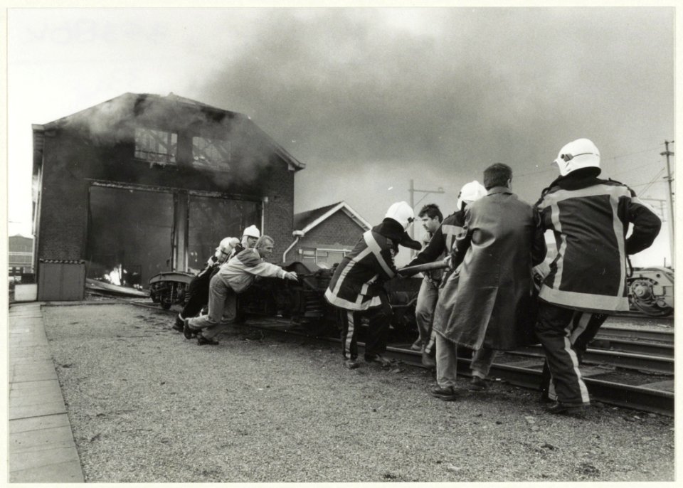 Een onderstel van een trein wordt naar buiten gesleept wegens brand in de asbestloods van de Hoofdwerkplaats van NS. NL-HlmNHA 54032046