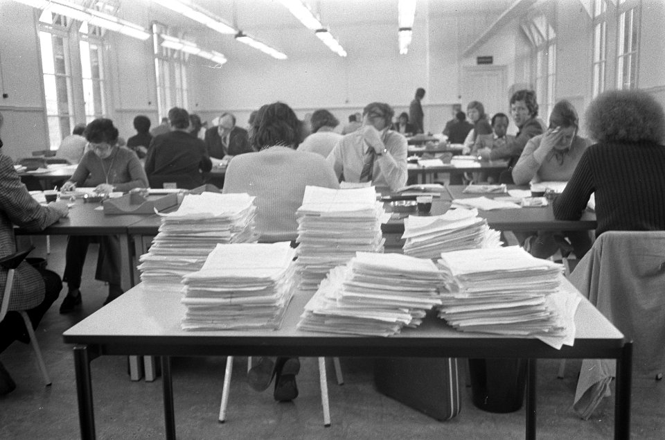 Een kantoorruimte met medewerkers, op de voorgrond een stapel aanvragen, Bestanddeelnr 926-9142