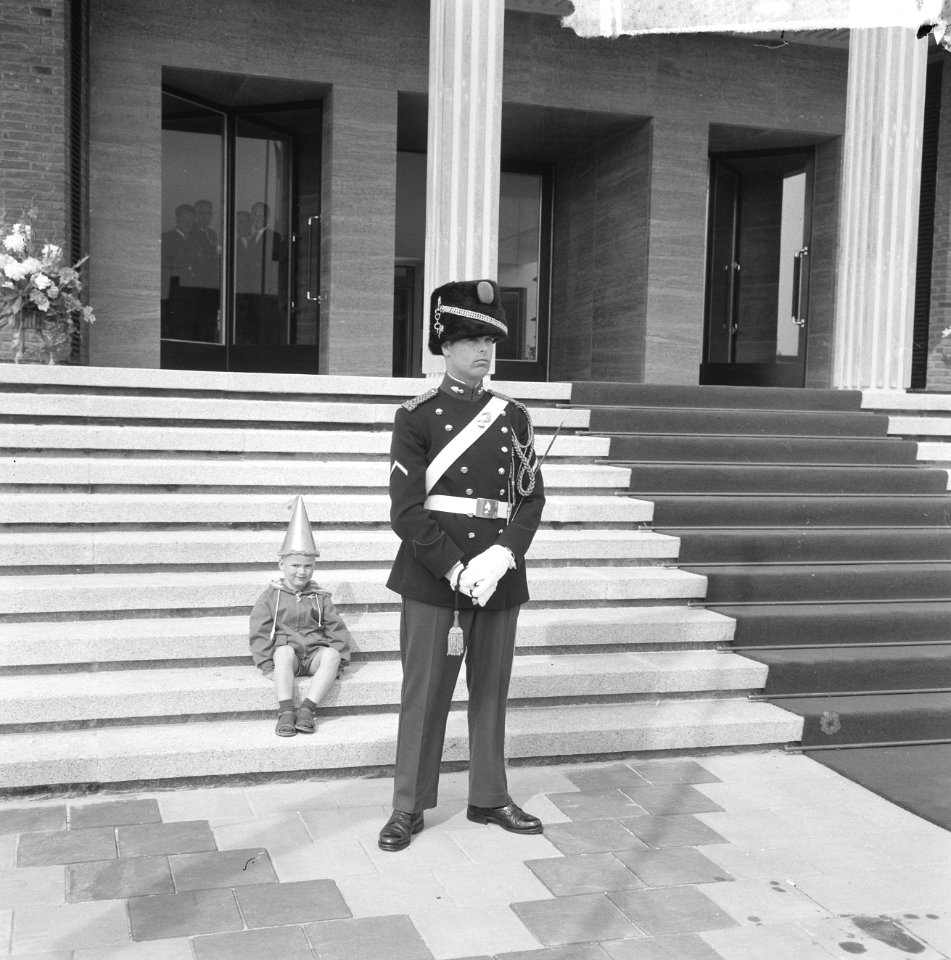 Een jongetje met feestmust zit op de trappen van het bordes van het stadhuis. Vo, Bestanddeelnr 917-7975