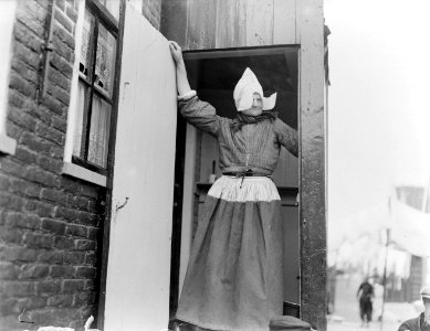 Een gezin in een straatje in Volendam moeder staat in klederdracht in de deurop, Bestanddeelnr 252-0675