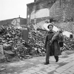 Een geallieerde militair met een bos bloemen loopt langs de puinhopen, Bestanddeelnr 900-6554