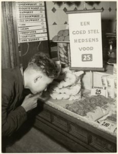 Een goed stel hersens voor 25 cent te koop aangeboden. Wat denkt deze jongeman voor de etalage van slagerij fa.J. Engelenberg Zou mij dit kunnen helpen, NL-HlmNHA 54004087