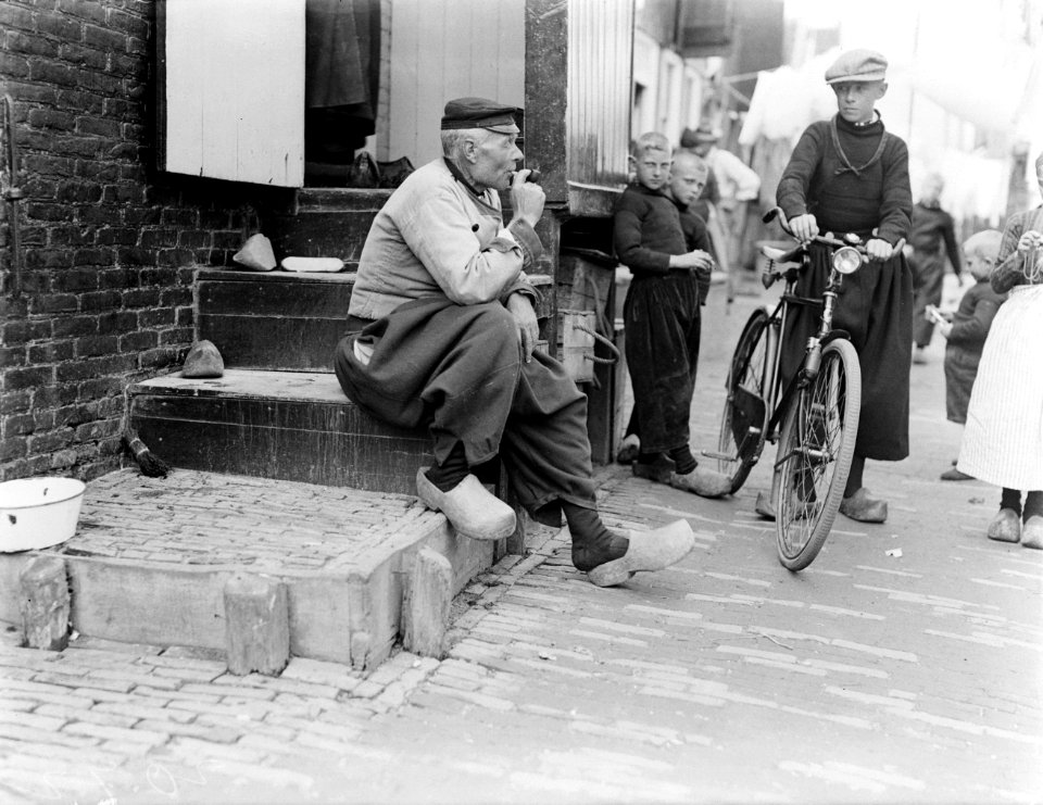 Een gezin in een straatje in Volendam vader zit op een stenen trapje en rookt z, Bestanddeelnr 252-0674