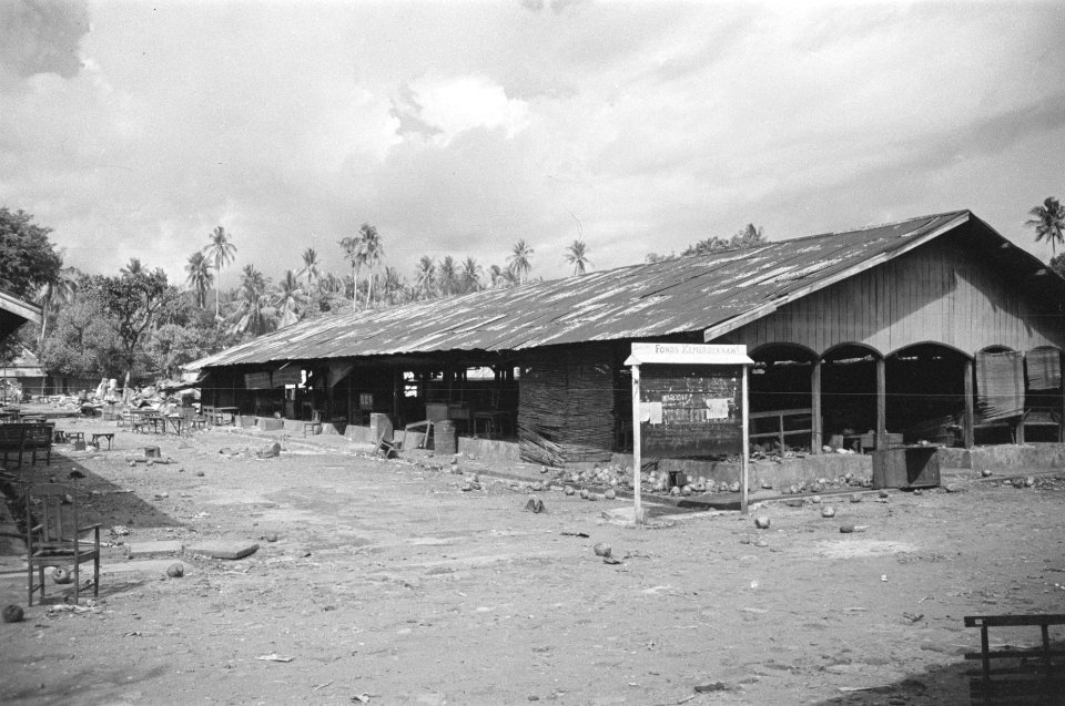 Fabrieksloodsen. Op de voorgrond een mededelingenbord met opschrift Fonds Kemer, Bestanddeelnr 324-3-2