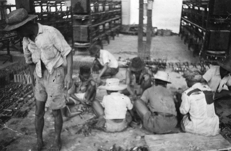 Fabriekshal Indonesische arbeiders zitten op de grond tussen onderdelen en gere, Bestanddeelnr 373-6-5
