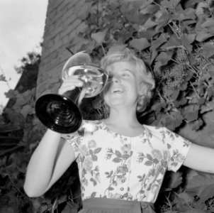 Erika Klein poseert met glas moezelwijn voor een muur begroeid met druiven, Bestanddeelnr 254-4640